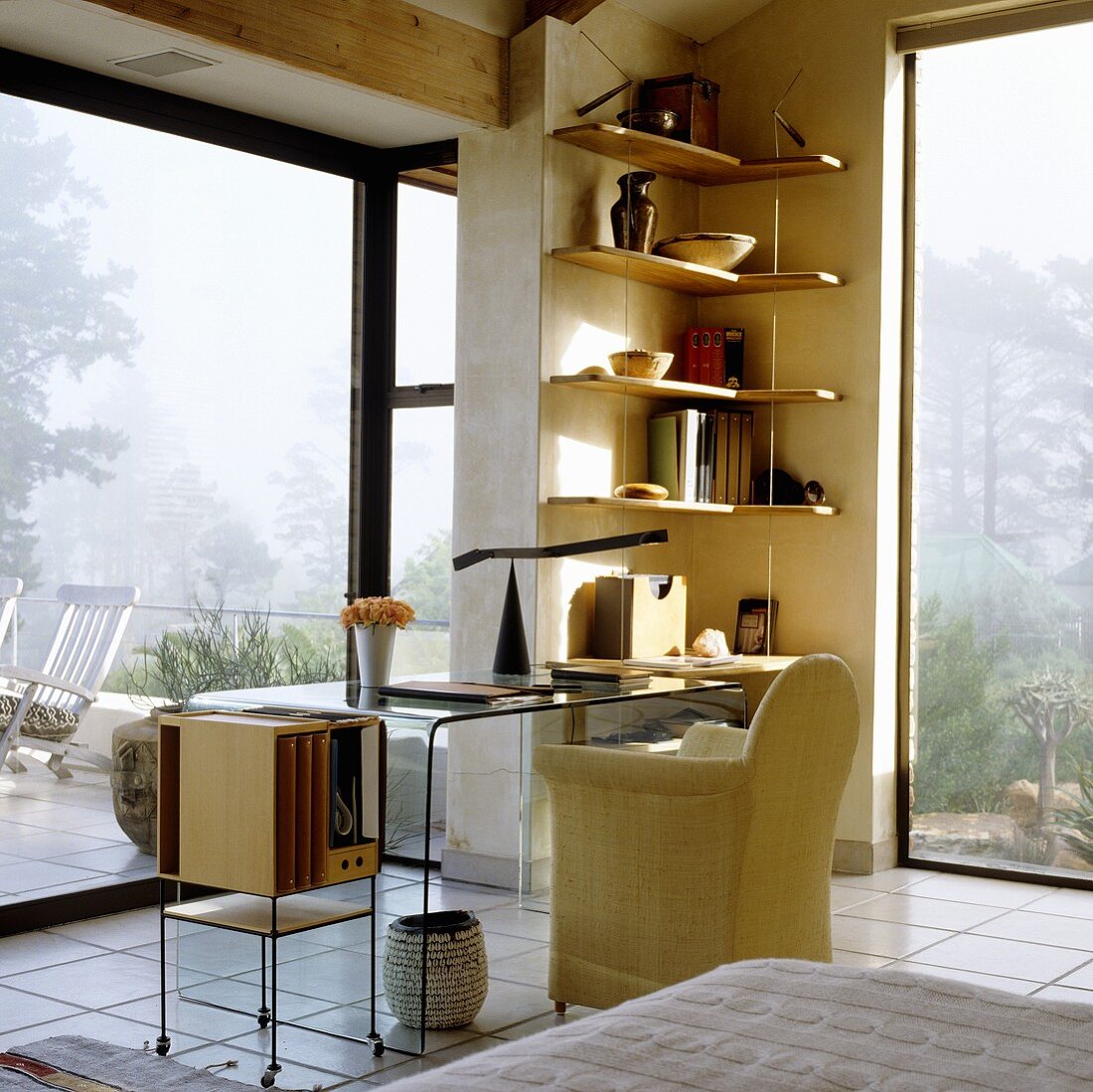 A desk with a panoramic view - an armchair and a glass table with a shelf in the corner of a room with floor-to-ceiling windows