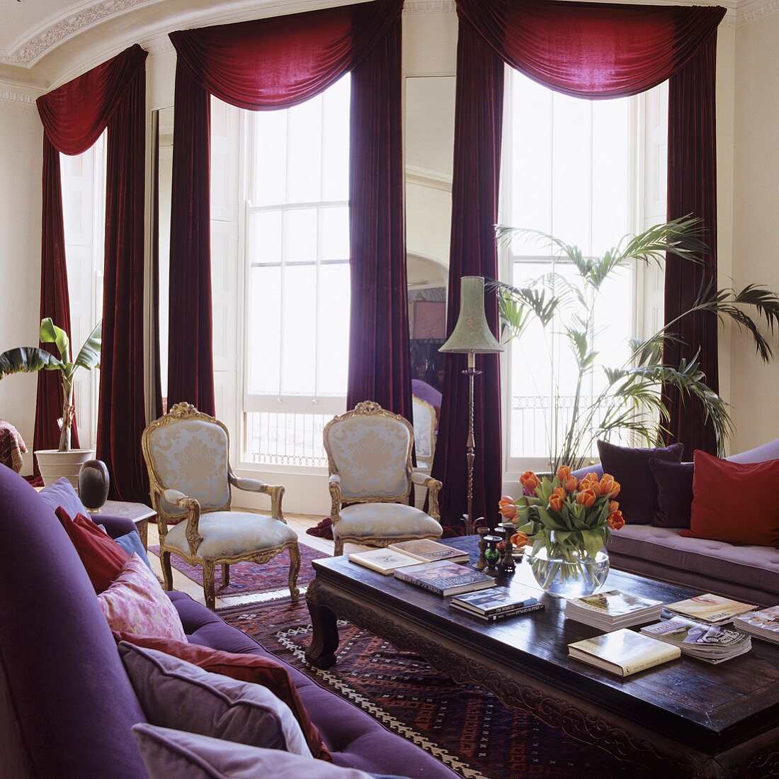 Luxuswohnraum mit Rokoko Stühlen vor roten Vorhängen an raumhohen Fenstern