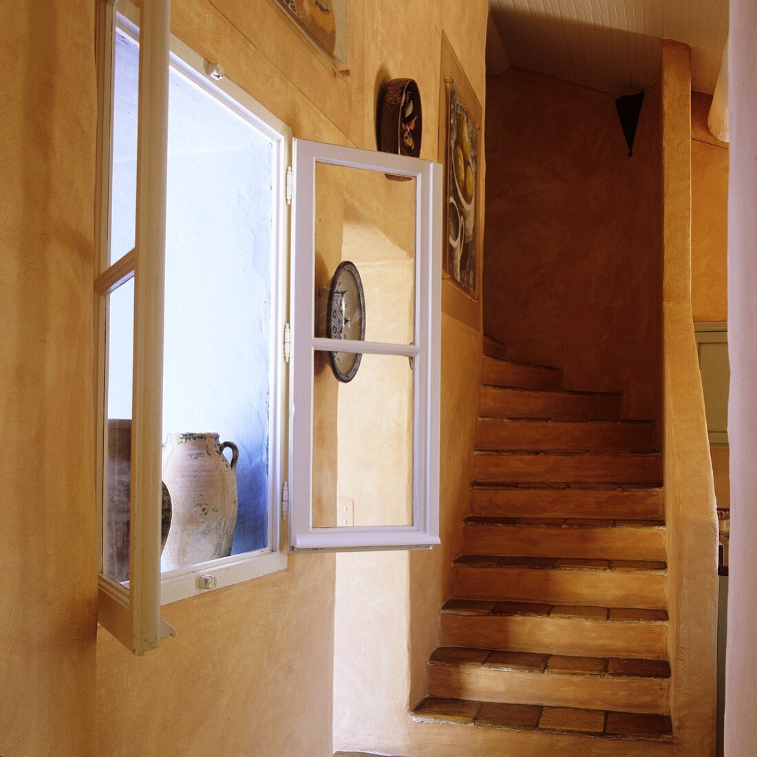 Geöffnetes Fenster in apricotfarbener Wand und Treppenaufgang im rustikalen Landhaus
