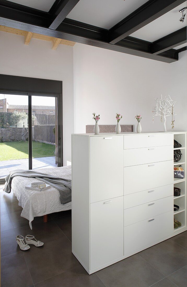 An open-plan bedroom with a low cupboard acting as a room divider in front of a bed and view of the garden