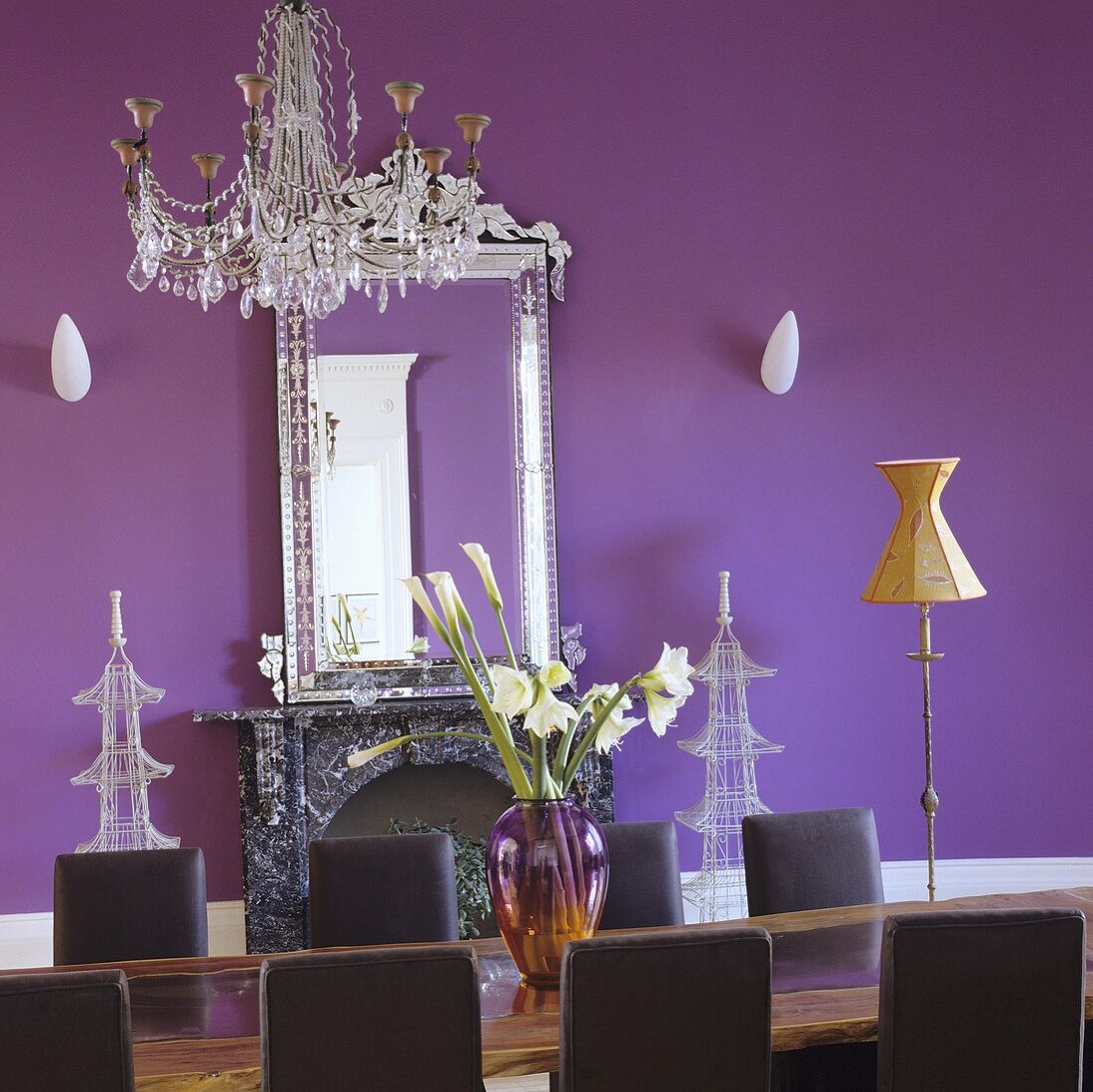 Lange Tafel mit Kronleuchter und Spiegel vor violetter Wand