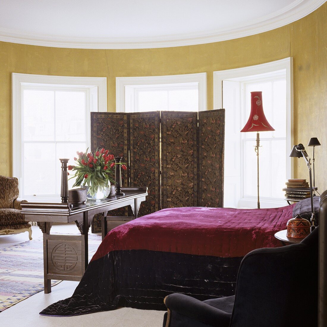 A turret bedroom with gold-painted walls and a paravent in front of the window
