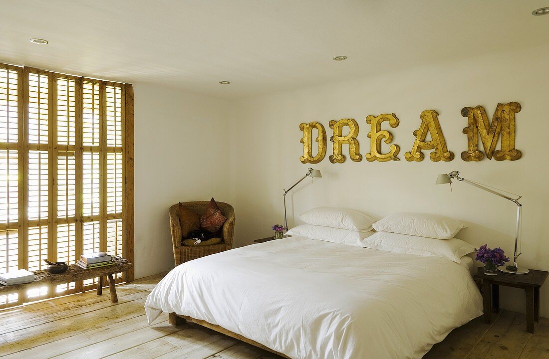 Schlafraum mit geschlossenen Holzjalousien - Bett mit weißem Bezug und englischer Schriftzug auf der Wand