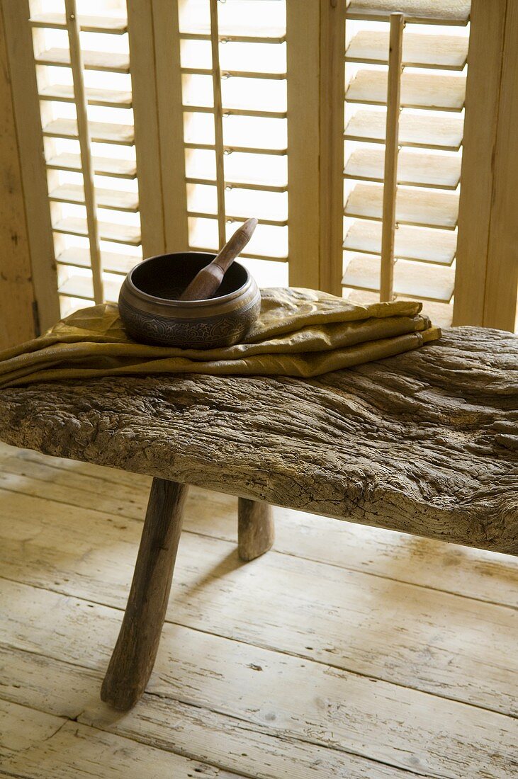 A wooden mortar on a rustic wooden bench in front of closed blinds