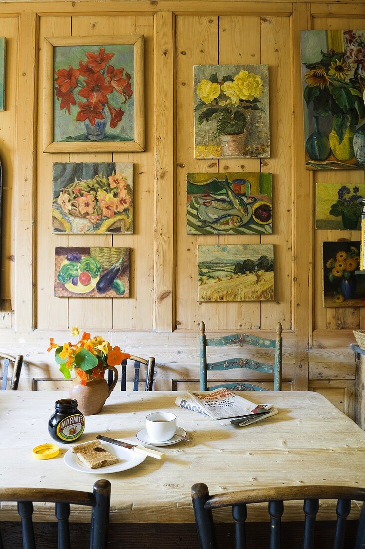 A dining table in front of a rustic wooden wall hung with a collection of pictures