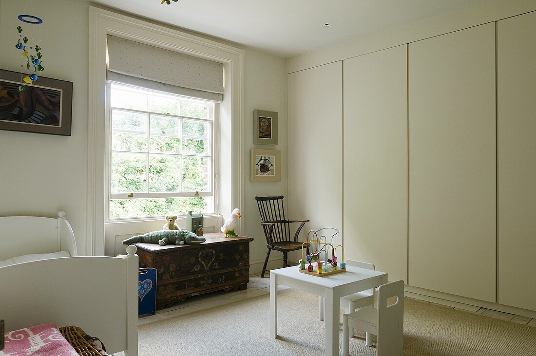 A child's room with a white built-in cupboard and a wooden chest in front of a window