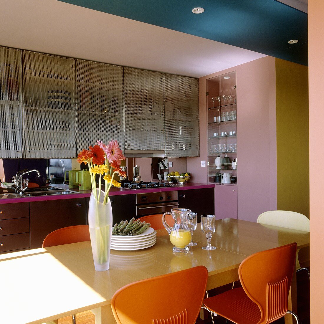 Orangefarbene Plastikstühle am Esstisch mit Blick auf offene Küche