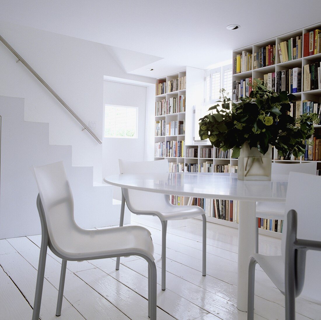 Runder Tisch mit Stühlen vor Bücherwand und Treppenaufgang