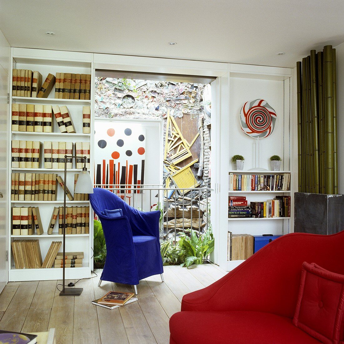 A living room with a blue chair and a built-in shelf with a view of an artistically designed wall in the courtyard
