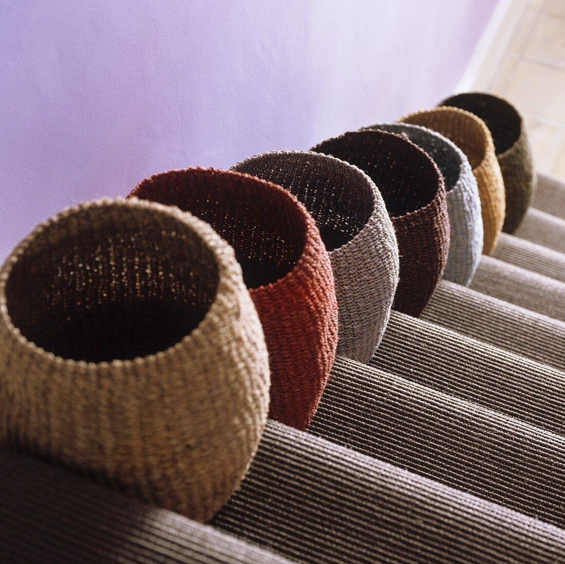 Various coloured sisal baskets on a flight of stairs with a carpet runner