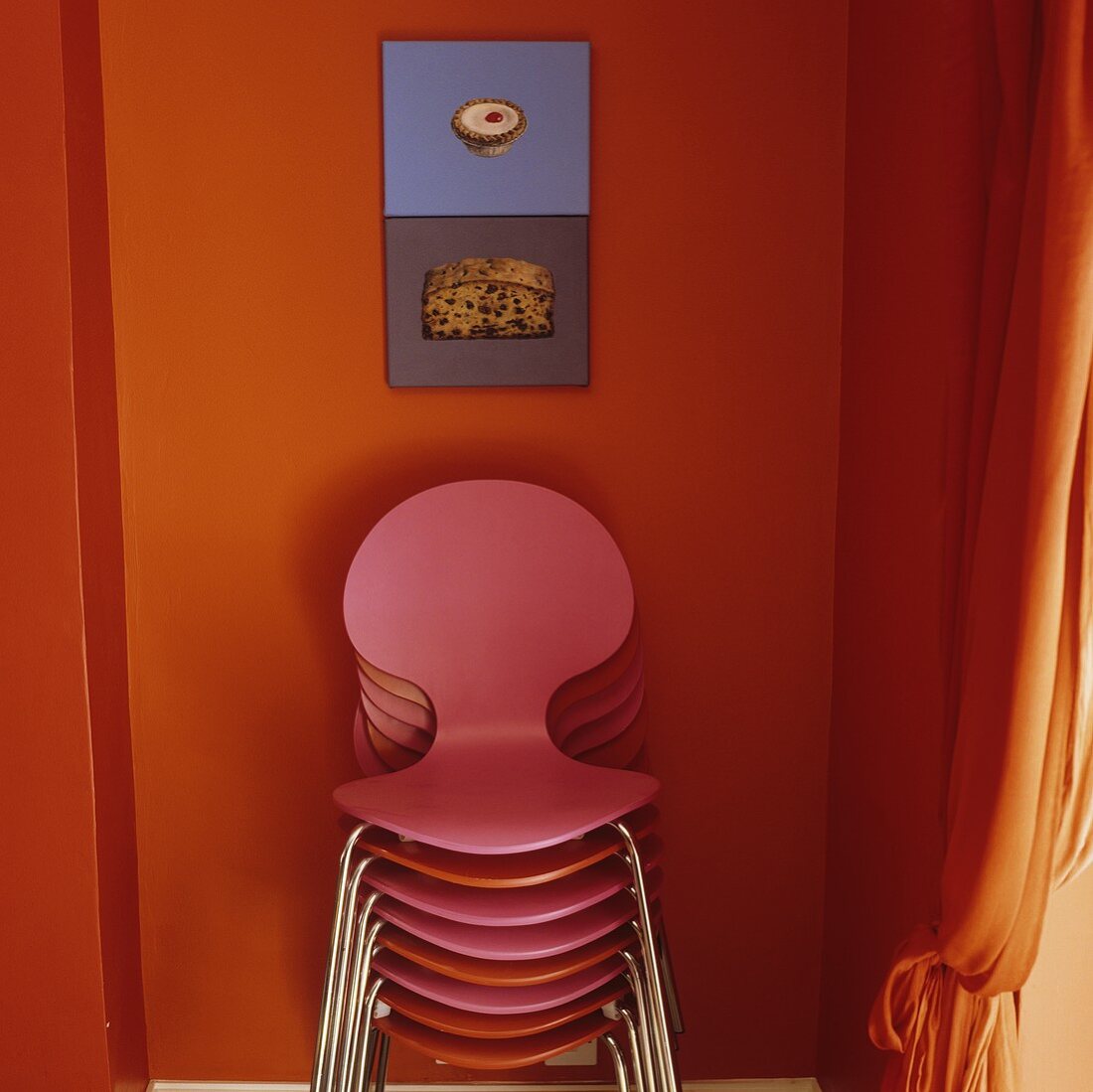Farbige Stühle gestapelt vor orangefarbener Wand