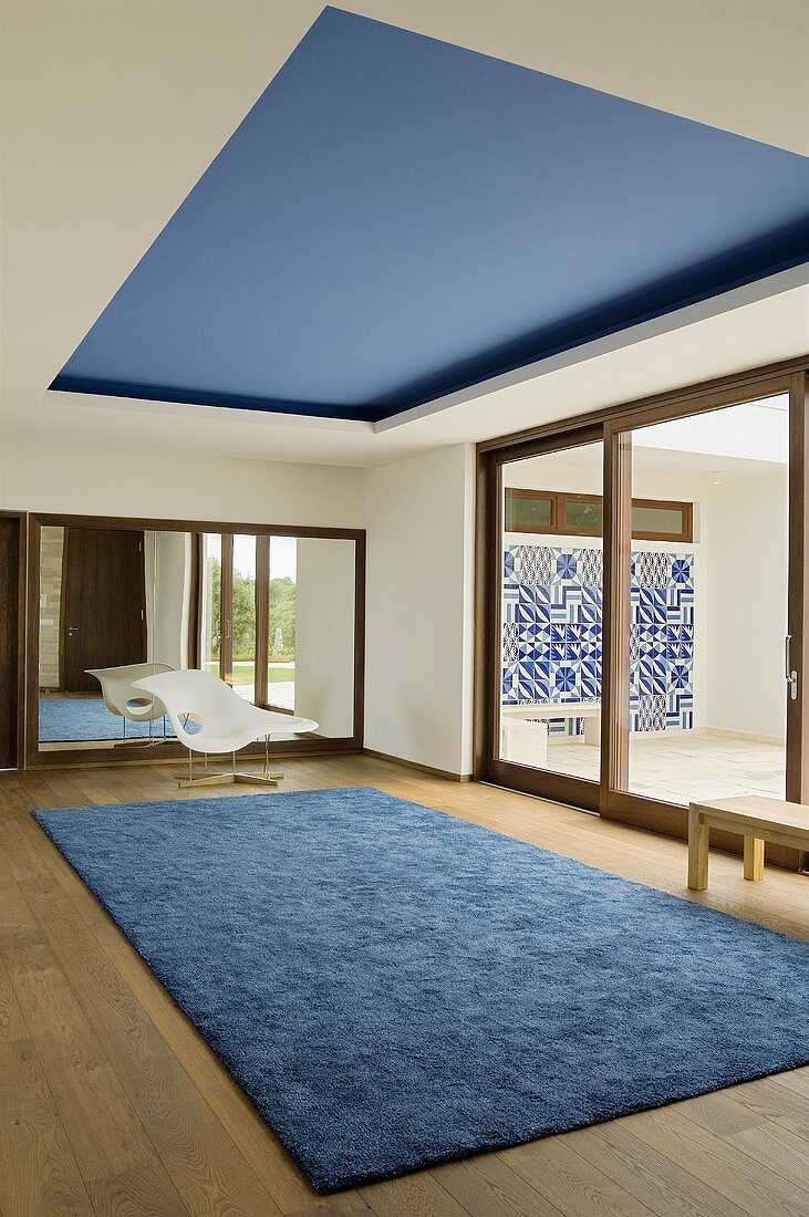 A minimalistic room - a blue rug on the floor boards and a blue-painted ceiling area
