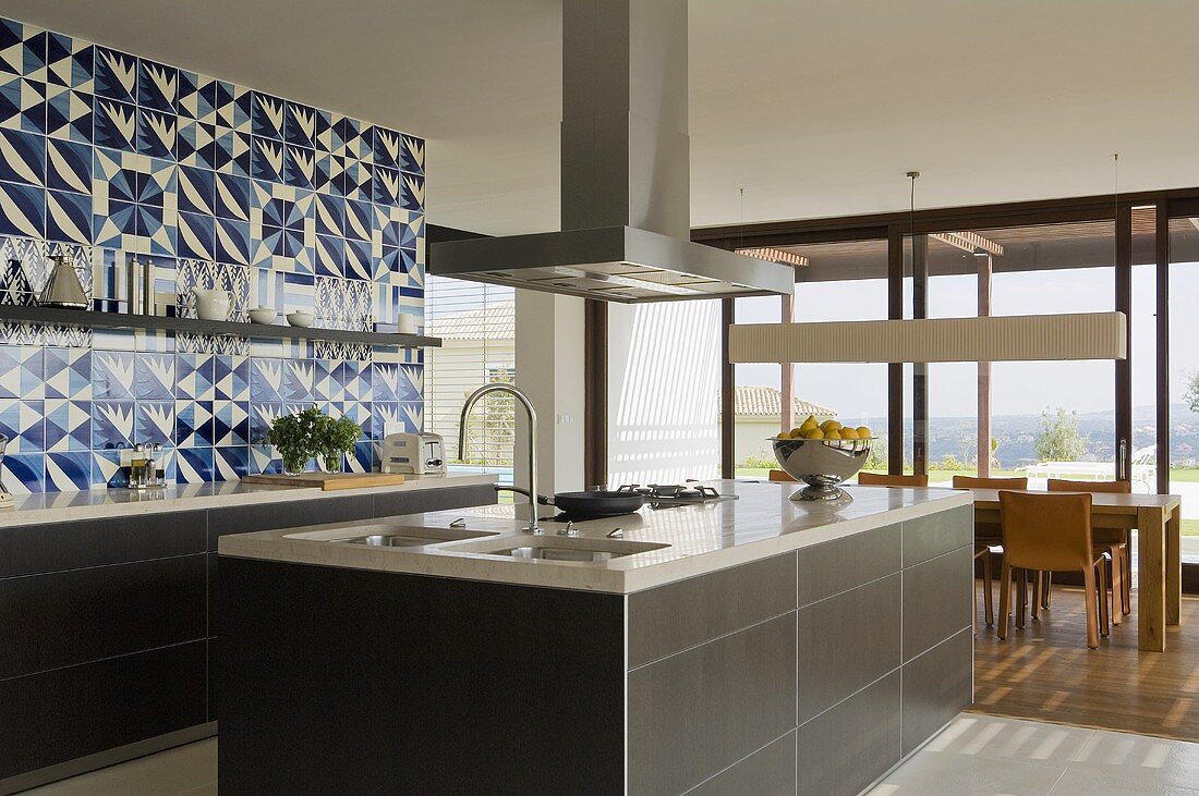 A designer kitchen - an island kitchen counter with an extractor fan with an open-plan living room in the background