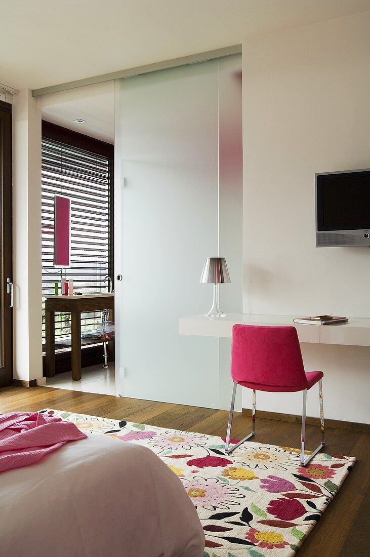 Opake Glaswand mit offener Schiebetür zum Bad und pinkfarbener Stuhl vor Wandablage mit Fernseher