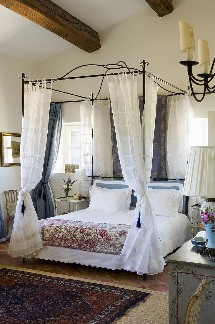 A bedroom in a country house with a metal four poster bed and light curtains