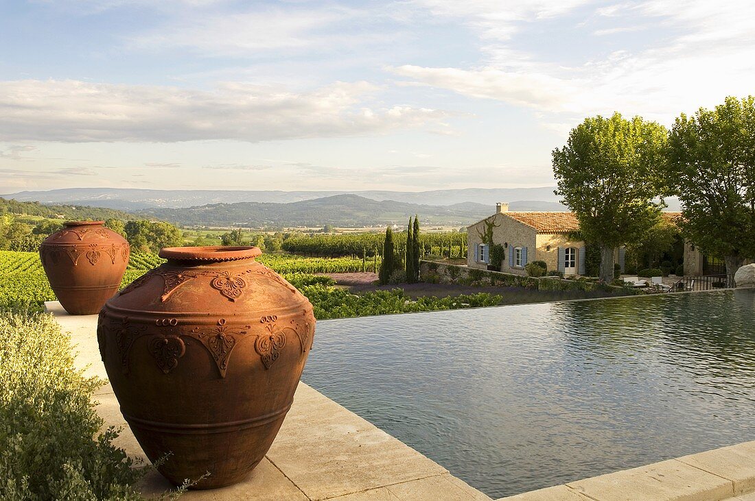 Amphorae by a pool with a view of a country house in the Mediterranean landscape