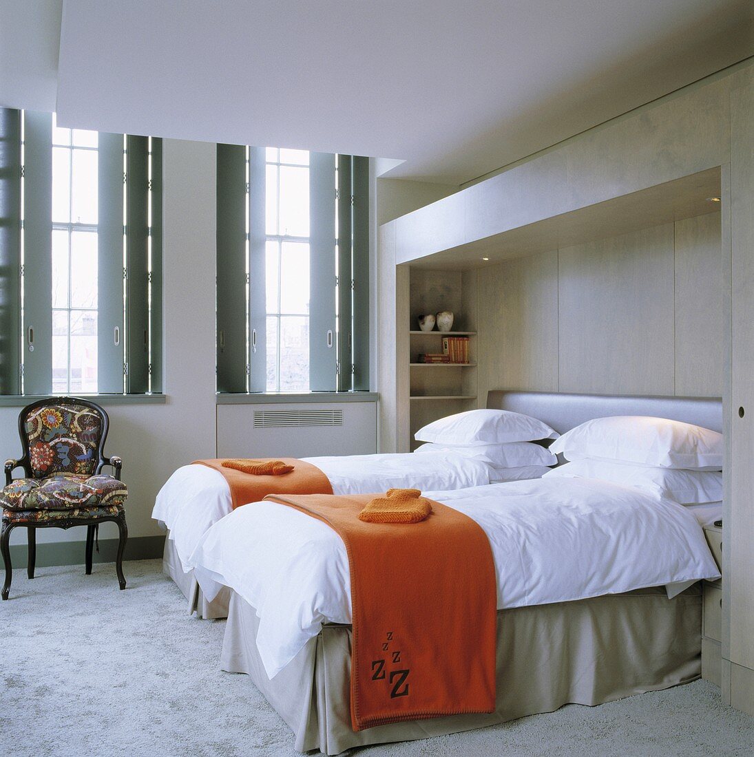 Orangefarbene Tagesdecke auf getrennt stehenden Betten und Fenster mit innenseitigen Läden