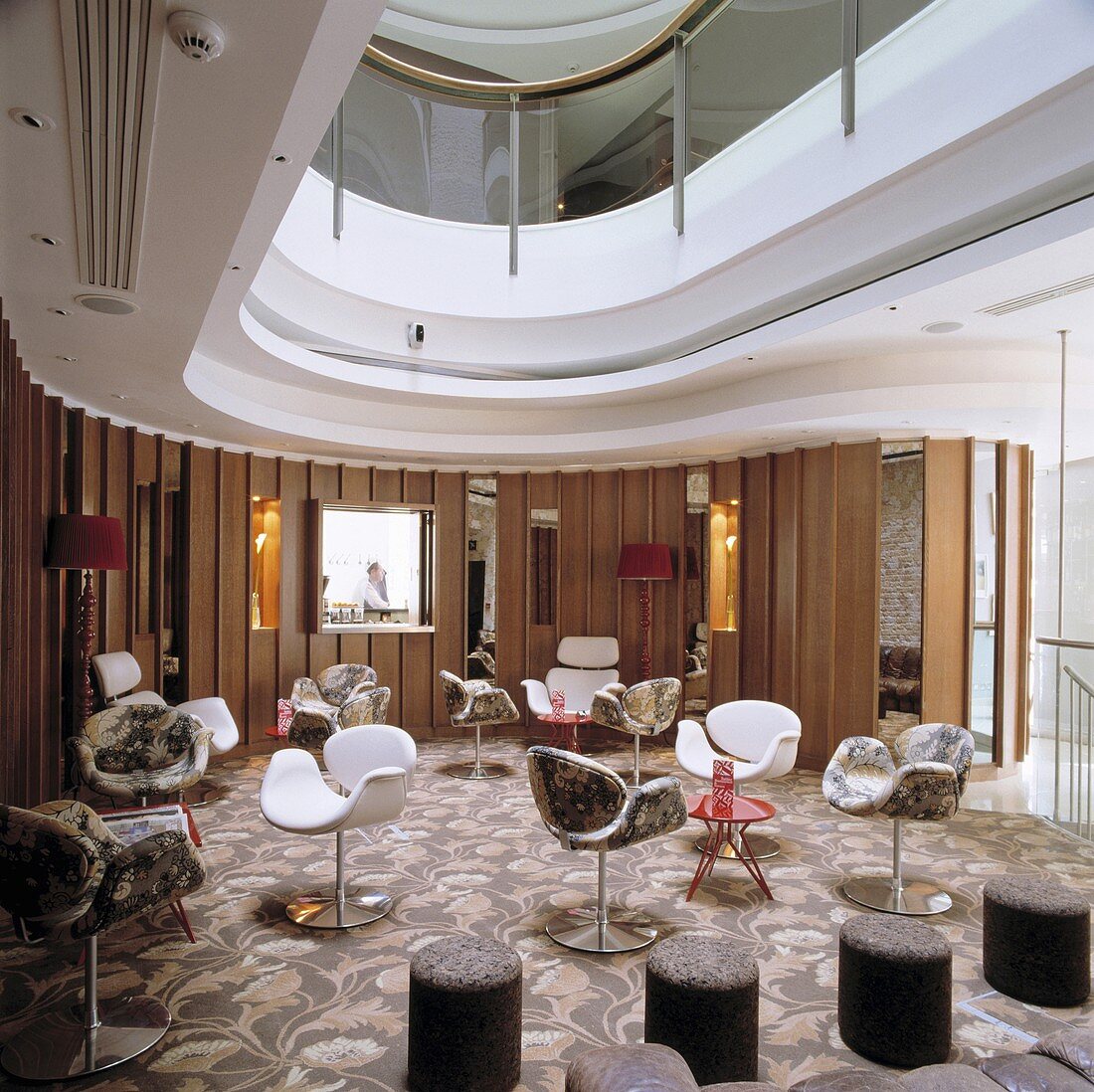 A hotel lobby on a landing with designer chairs and bistro tables on a floral patterned carpet
