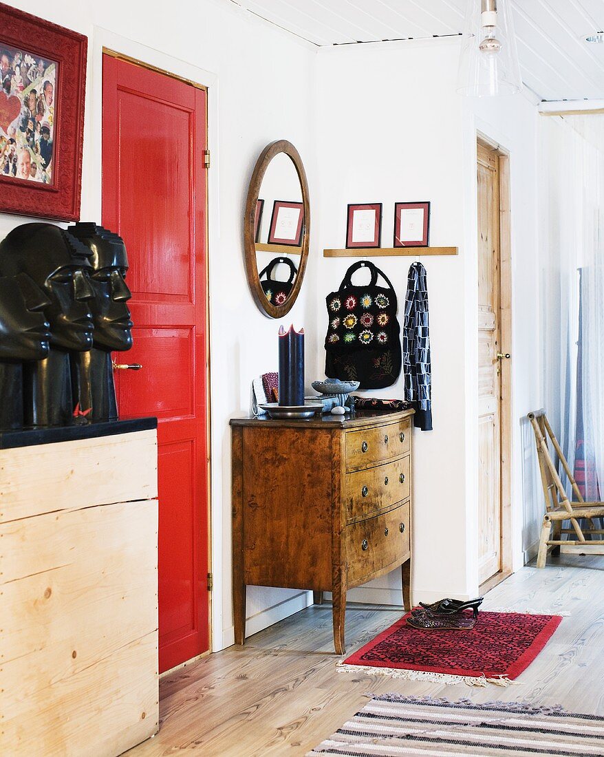 A hallway in an apartment with a red door and a wooden chest of drawers