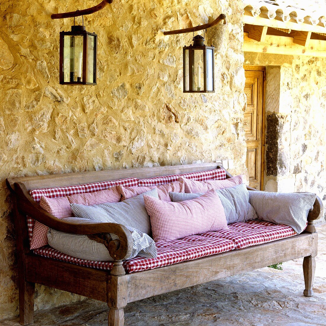 A Mediterranean country house - a rustic bench with checked upholstery and lanterns hanging on the exterior, natural stone walls