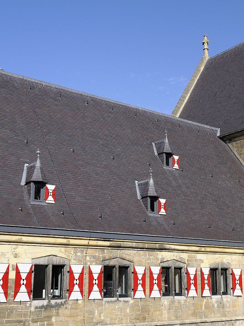 Steinfassade eines Klosters mit rot-weissen Fensterläden und Dachflächen mit Gauben und grauen Ziegeln