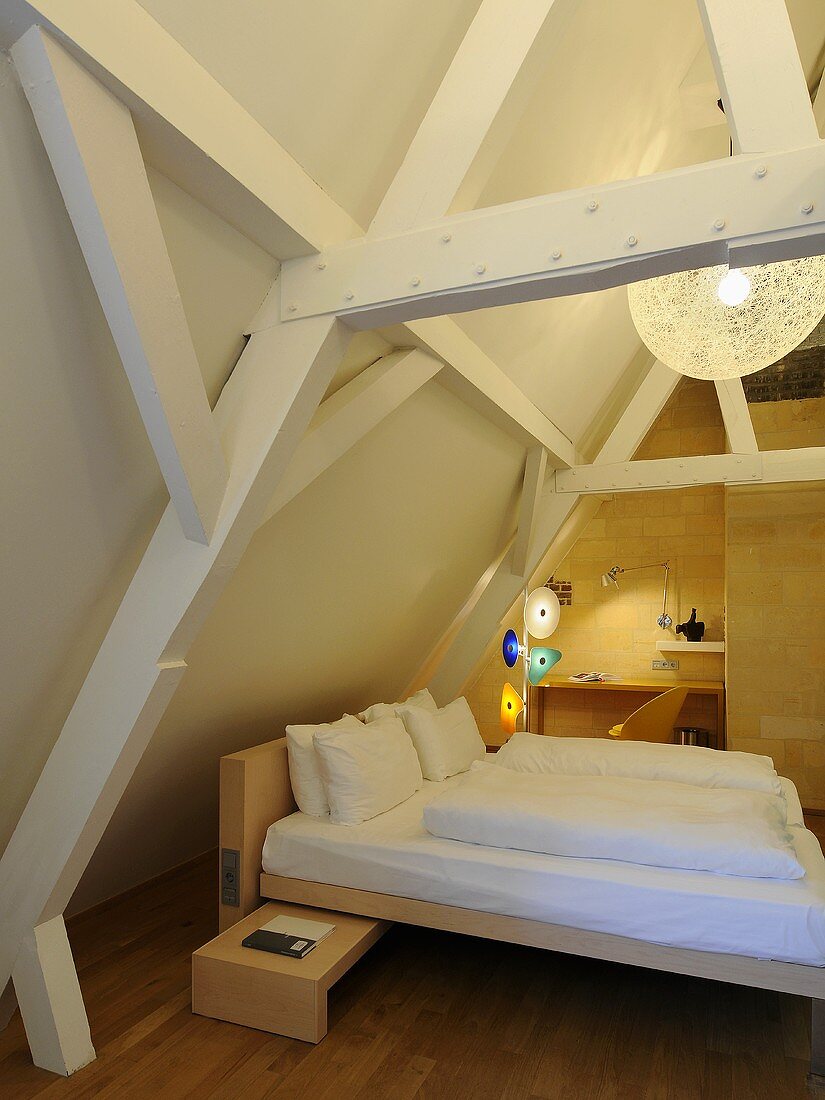 A designer wooden bed in an attic room with wooden beams