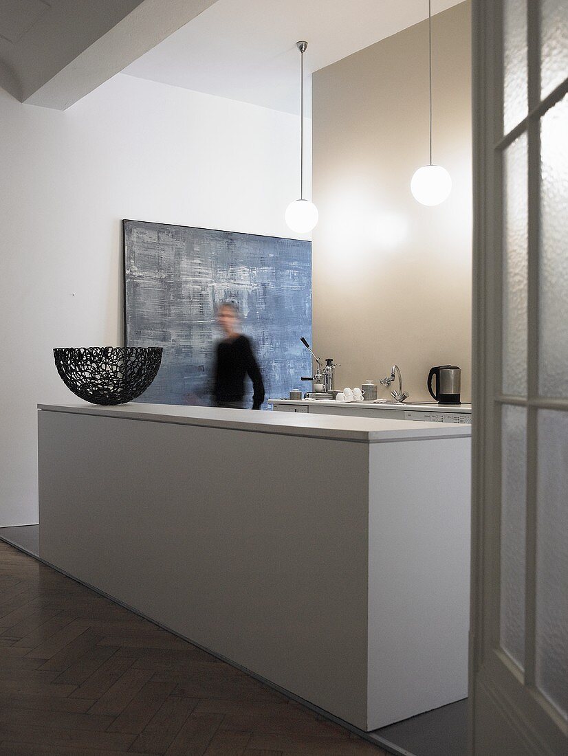 Offene Küche im minimalistischen Vorraum - weiße monolithische Küchentheke und Mann im Flur