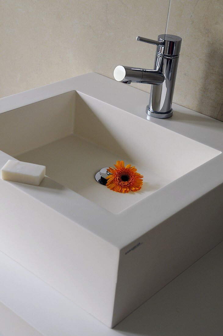Designer Waschbecken mit Armatur und orangfarbener Blütenkopf einer Gerbera