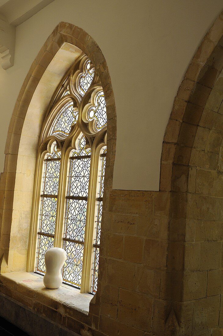 Gotischer Spitzbogen mit buntem Fensterglas und Skulptur auf Fensterbank