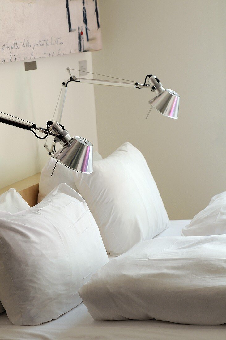 Designer reading lamps with metal shades attached to a bed