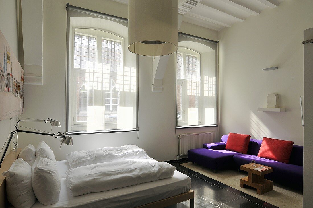 Designter Schlafraum mit farbiger Sitzecke vor Fensterfront und transparentem Rollo