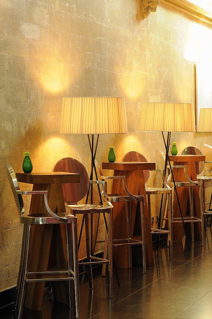 Illuminated bar tables - designer bar tables with stools and floor lamps in front of a natural stone wall