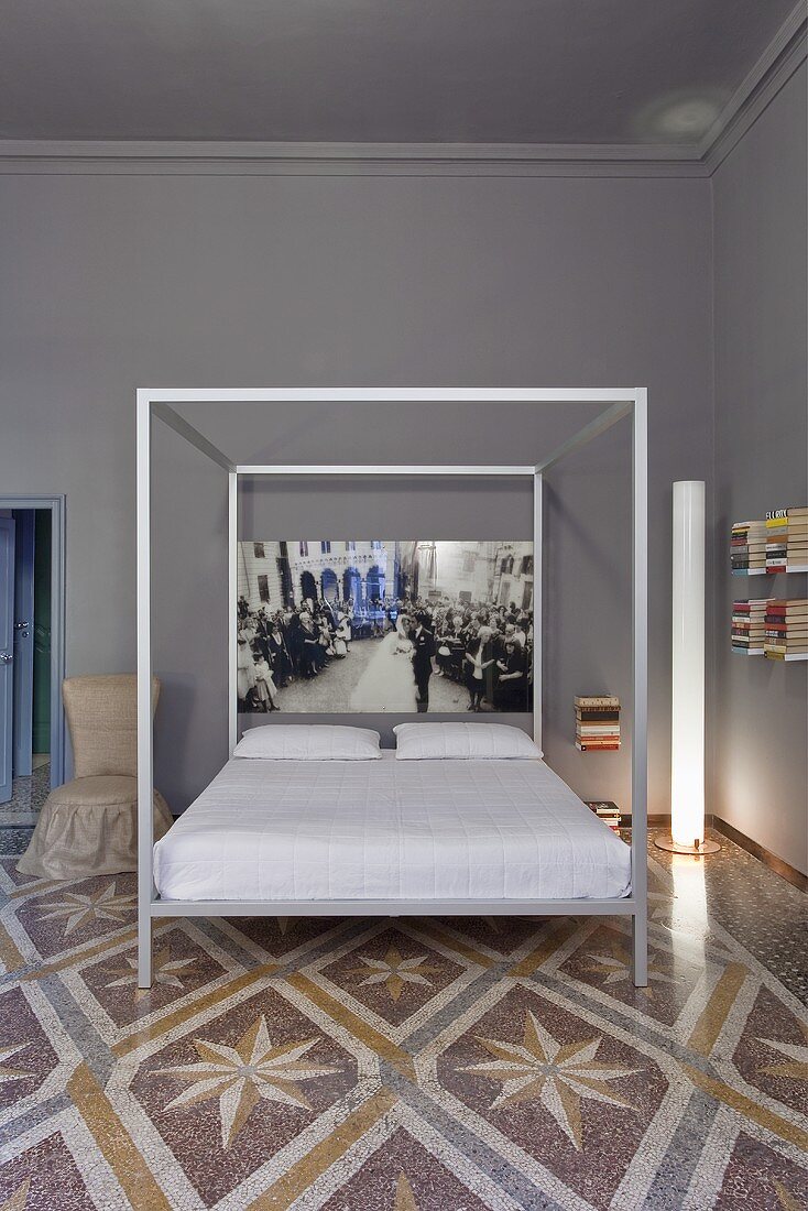 A designer four poster bed against a grey wall on a patterned terrazzo floor