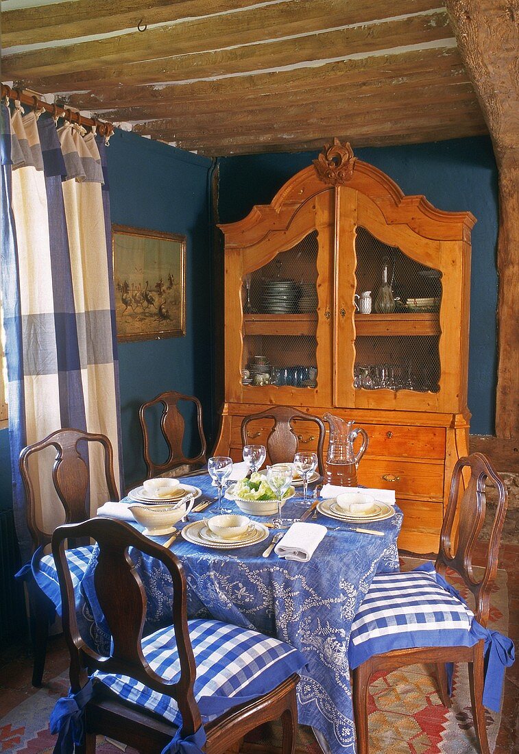 Essen im Bauernhaus - antike Vitrine vor blauer Wand und Holzbalkendecke