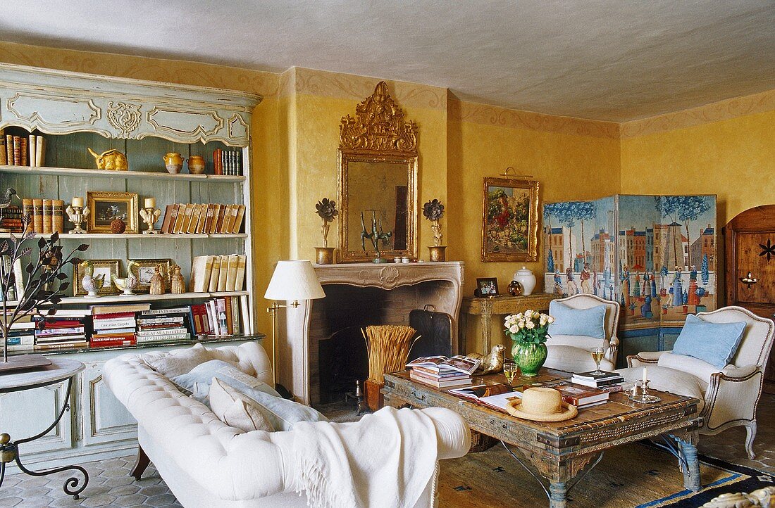 A yellow-painted living room in a country house with a sofa and a and coffee table in front of a fireplace