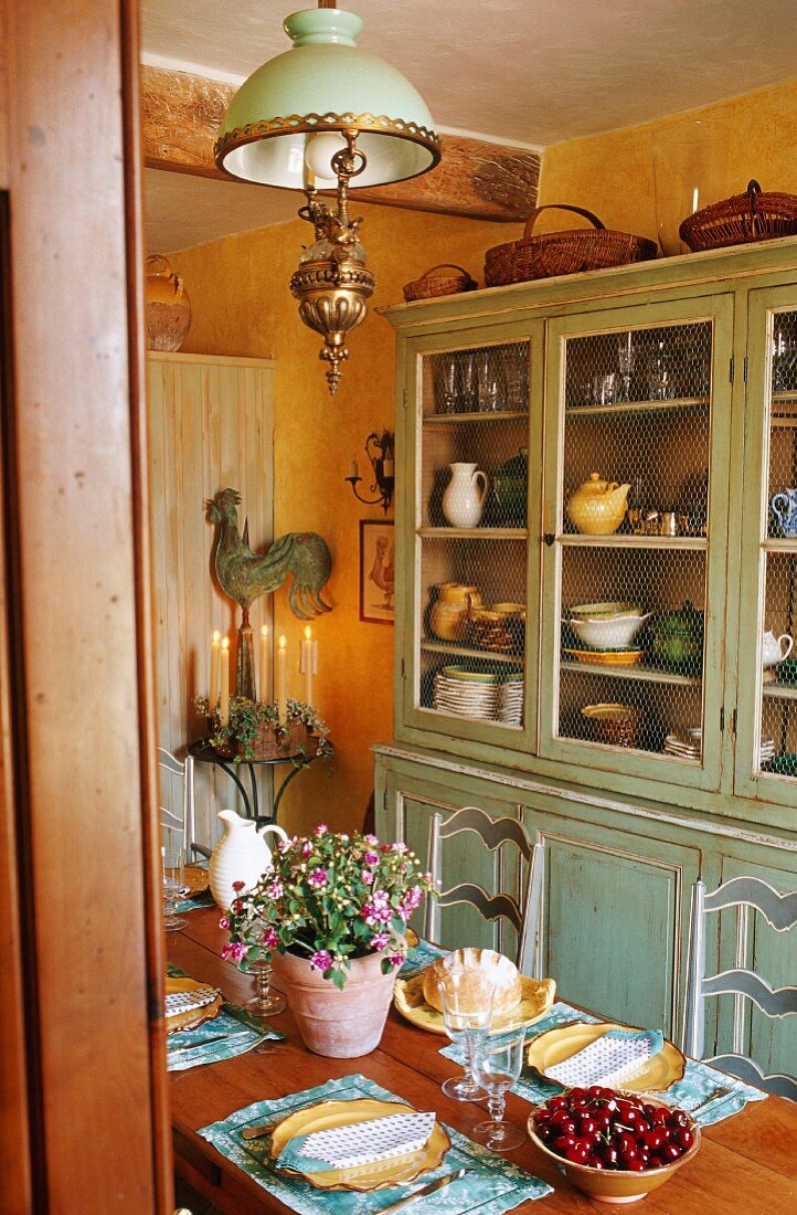 A table laid for a meal in a country house with a kitchen dresser with crockery and an antique ceiling lamp