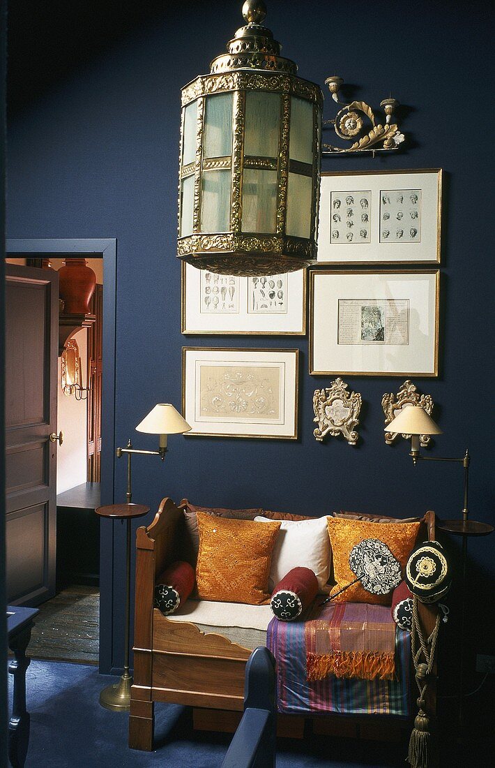 An oriental pendent lamp and an antique wooden bench with cushions in front of a dark grey wall
