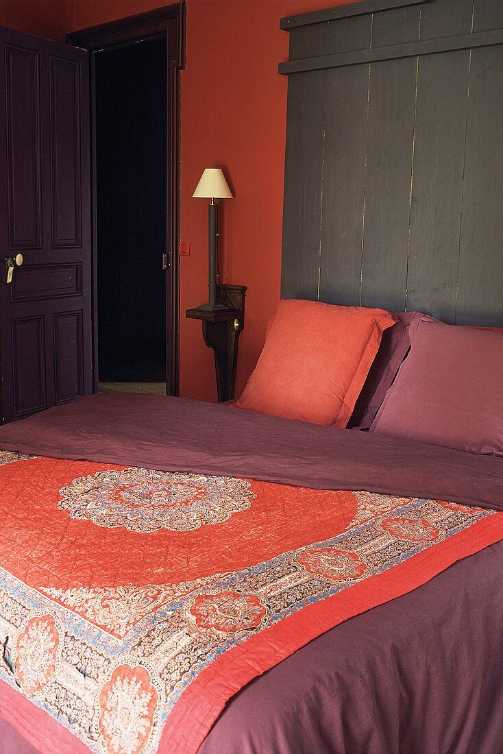 Bett mit orientalischer Tagesdecke und ziegelroter Wand