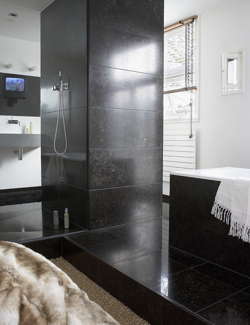 A designer bathroom - a pillar with a shower head and taps and a bathtub with grey stone tiles