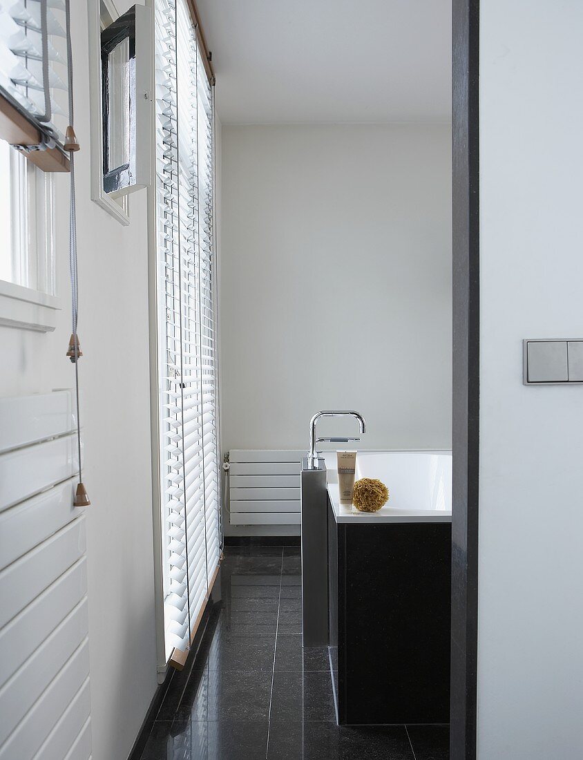A view into a designer bathroom with a free-standing tap, a bathtub and grey floor tiles