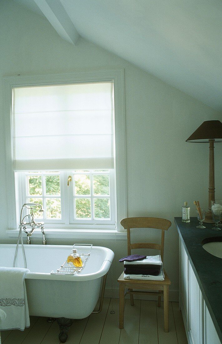 A bathroom with an antique bathtub under the window with a half-closed blind