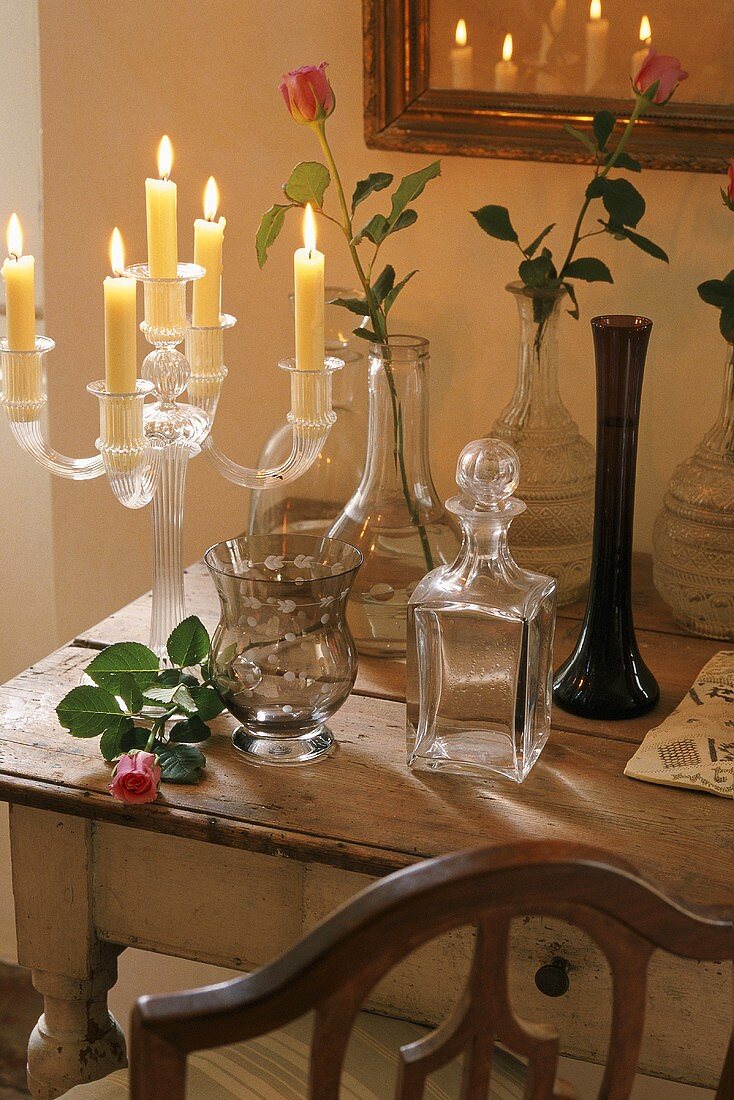 Burning candles in a glass candlestick and vases on a rustic wooden table