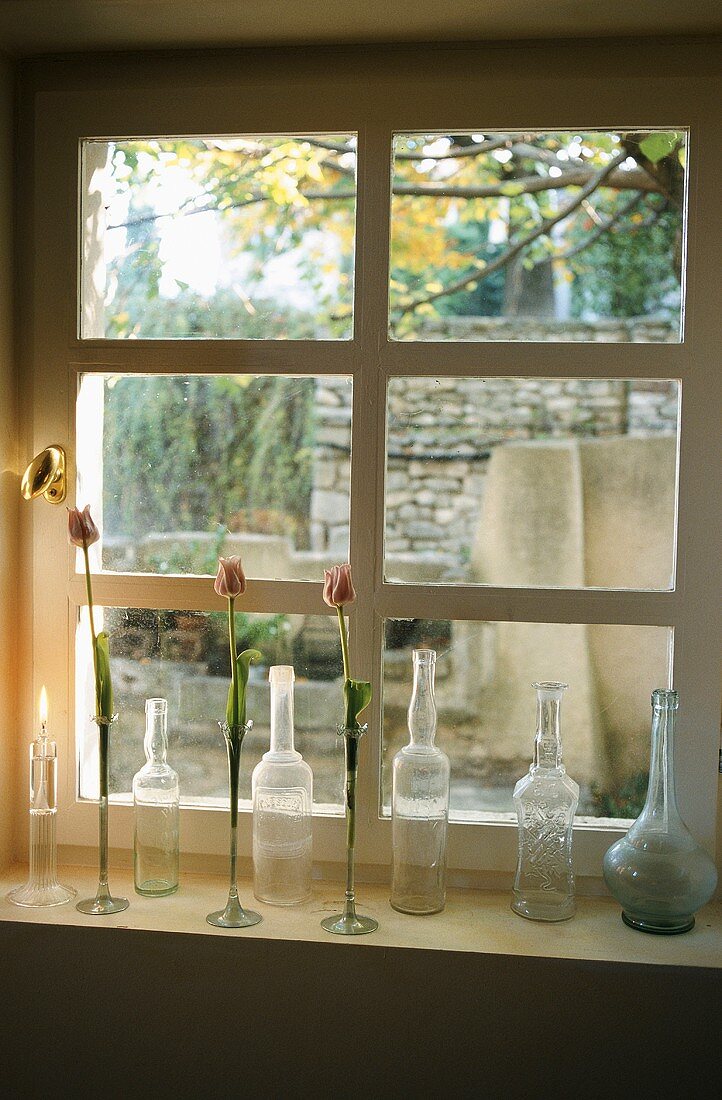 An arrangement on a window sill - old bottle and vases of flowers against a transom window