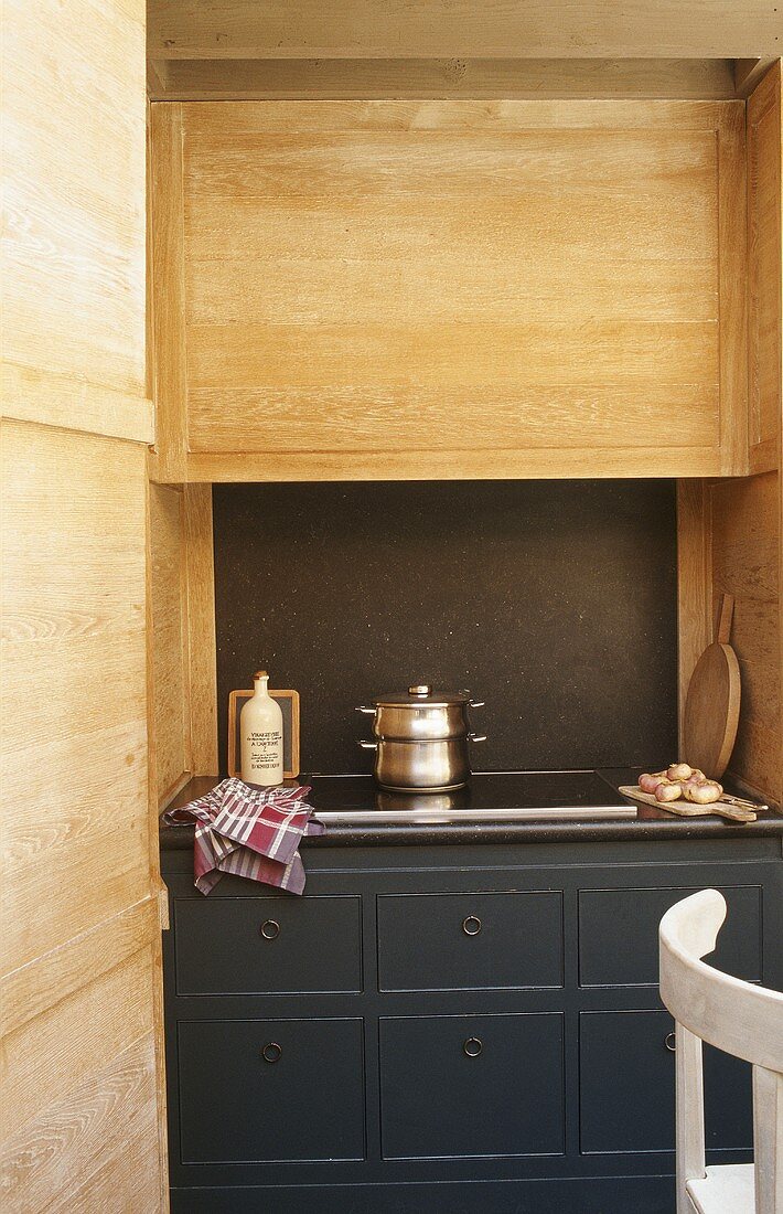A hob built in to a grey floor cupboard with drawers and an extractor fan with a wooden facing