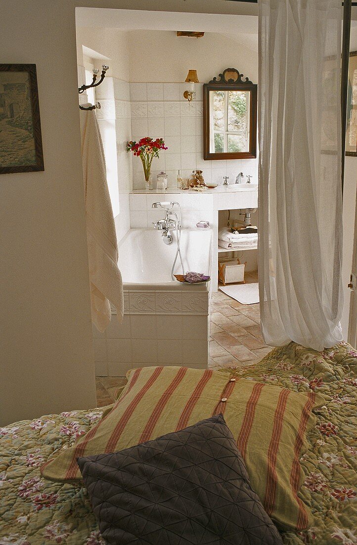 Kissen auf Bett und Blick auf offenes Bad mit Badewanne und luftigem Vorhang