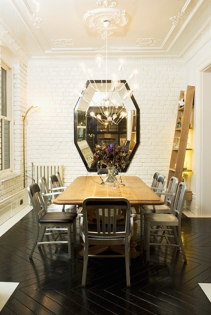 Holztisch mit grauen Stühlen vor weiss getünchter Ziegelwand und Spiegel