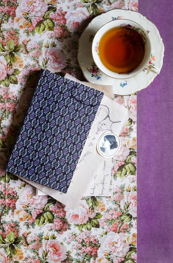 Tasse Tee neben Buch mit gemustertem Einband auf Papier mit Blumenmuster