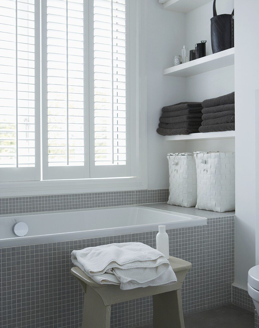 Bathtub with gray mosaic tiles in from of a window with closed blinds