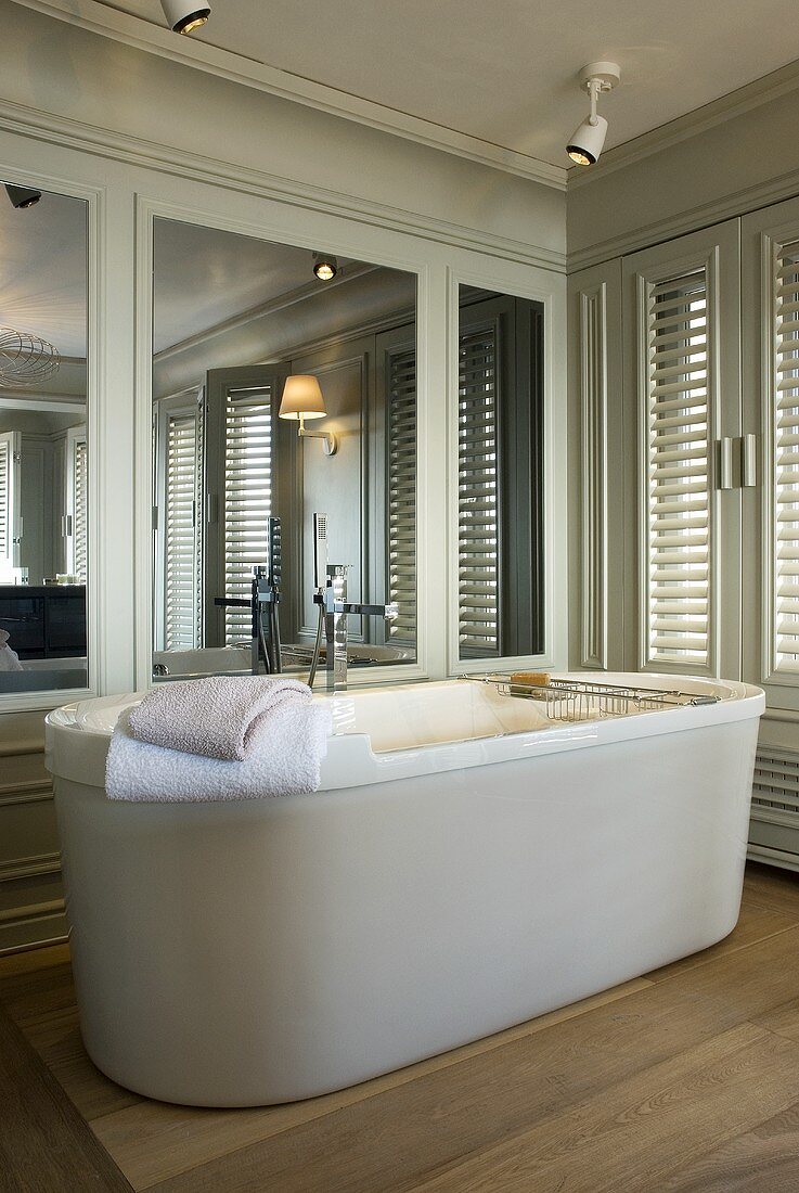 Freistehende Badewanne vor grauer Holzvertäfelung mit Spiegel