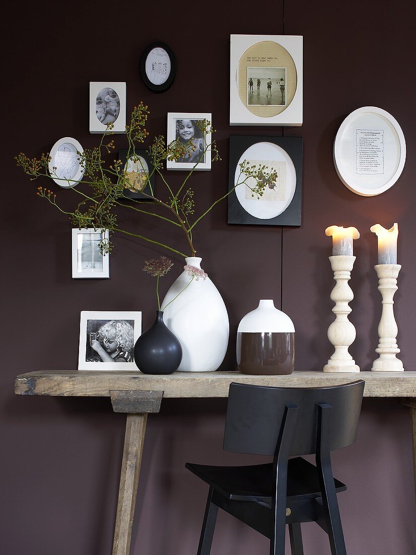 Ceramic vases and candlesticks on a rustic wall table in front of a dark-red wall
